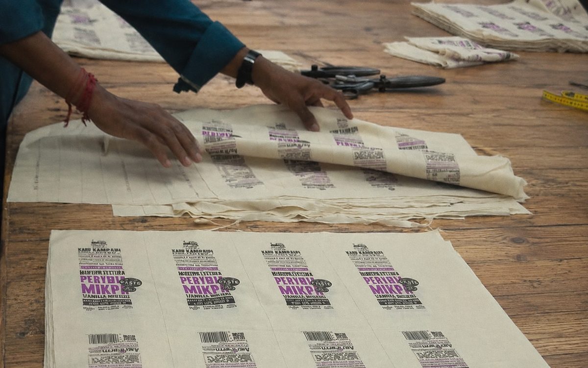 Hands laying out printed woven cotton bags on a workbench beside shears
